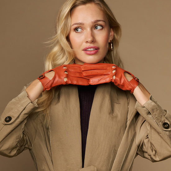 Women's orange lambskin driving gloves laid across wrists, snap-button cuffs