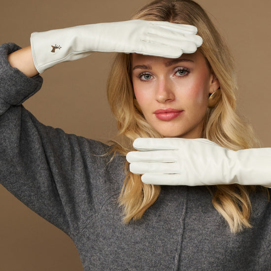 White long leather gloves with touchscreen fingertips, worn and posed across frame