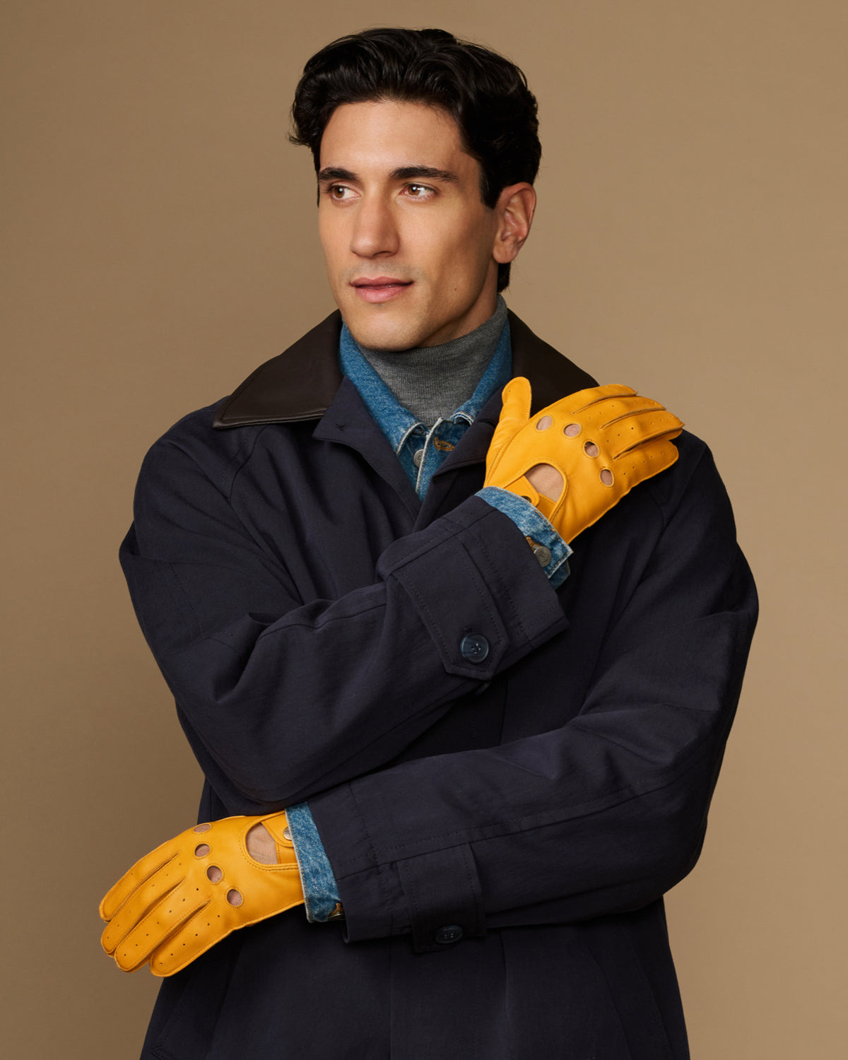 Men's yellow lambskin driving gloves worn with a navy coat, perforated knuckles
