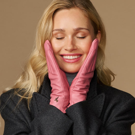 Women’s pink leather gloves covering hands near face, showing clean stitched fingertips