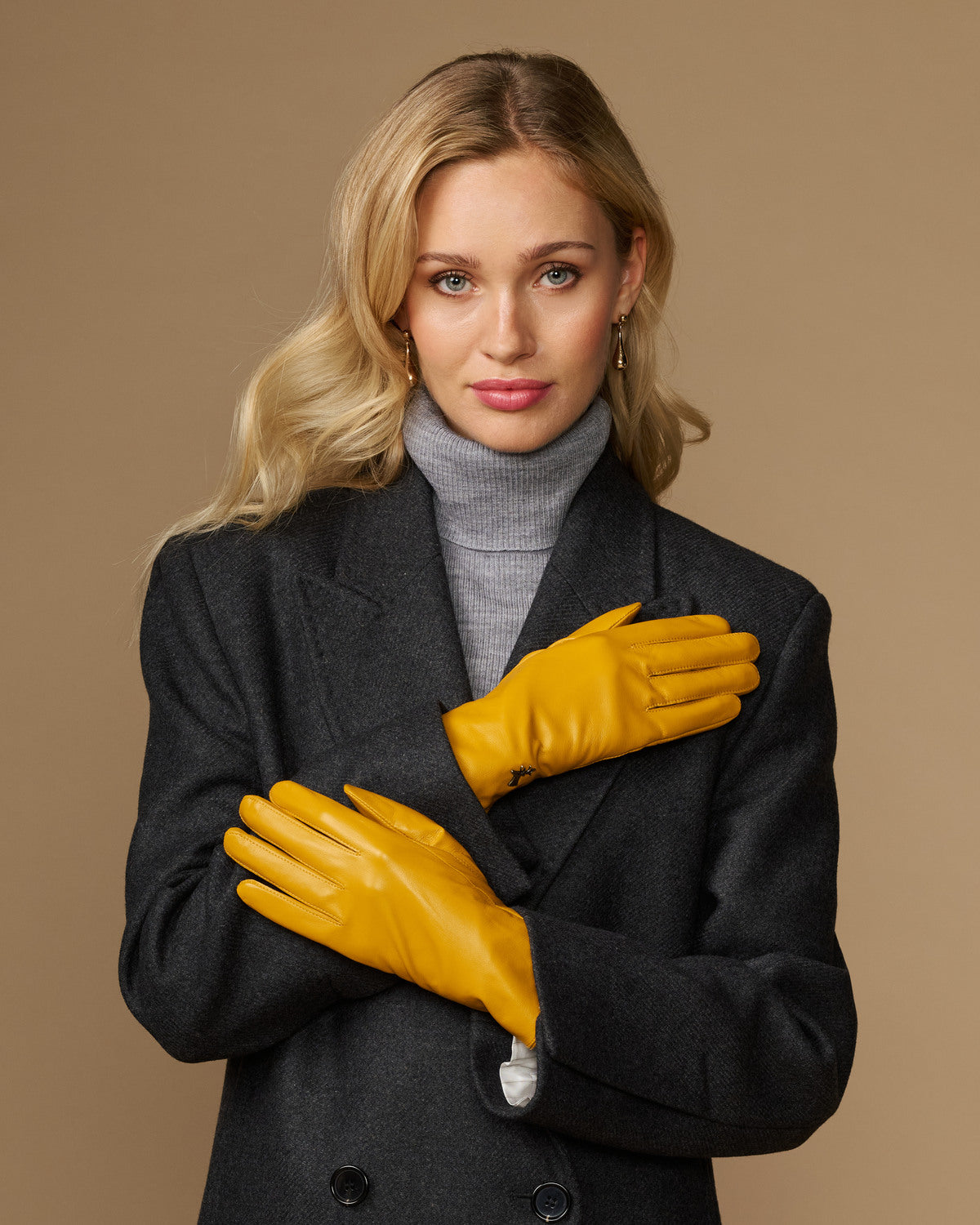 Yellow leather gloves with stitched knuckles, fitted wrist cuff, and small emblem detail