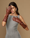 Cognac leather below-elbow gloves with glossy texture, hands positioned near face