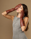 Cognac leather below-elbow gloves with curved fit, hands posed near head