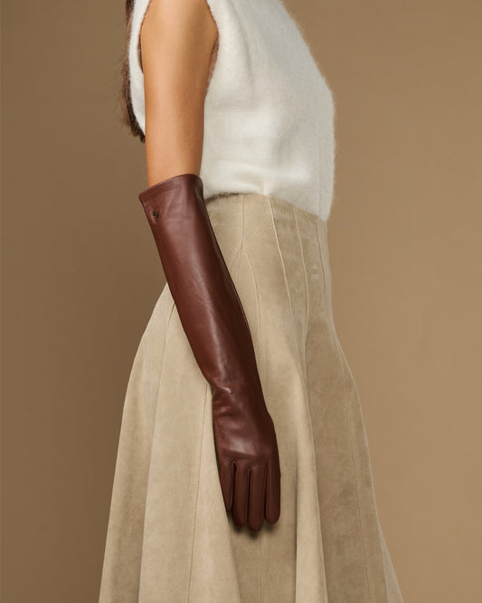 Elbow-length brown leather glove worn at side, with soft cuff detail.
