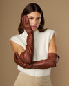 Chestnut brown lambskin opera gloves stacked at the wrist, sleek finish and seams