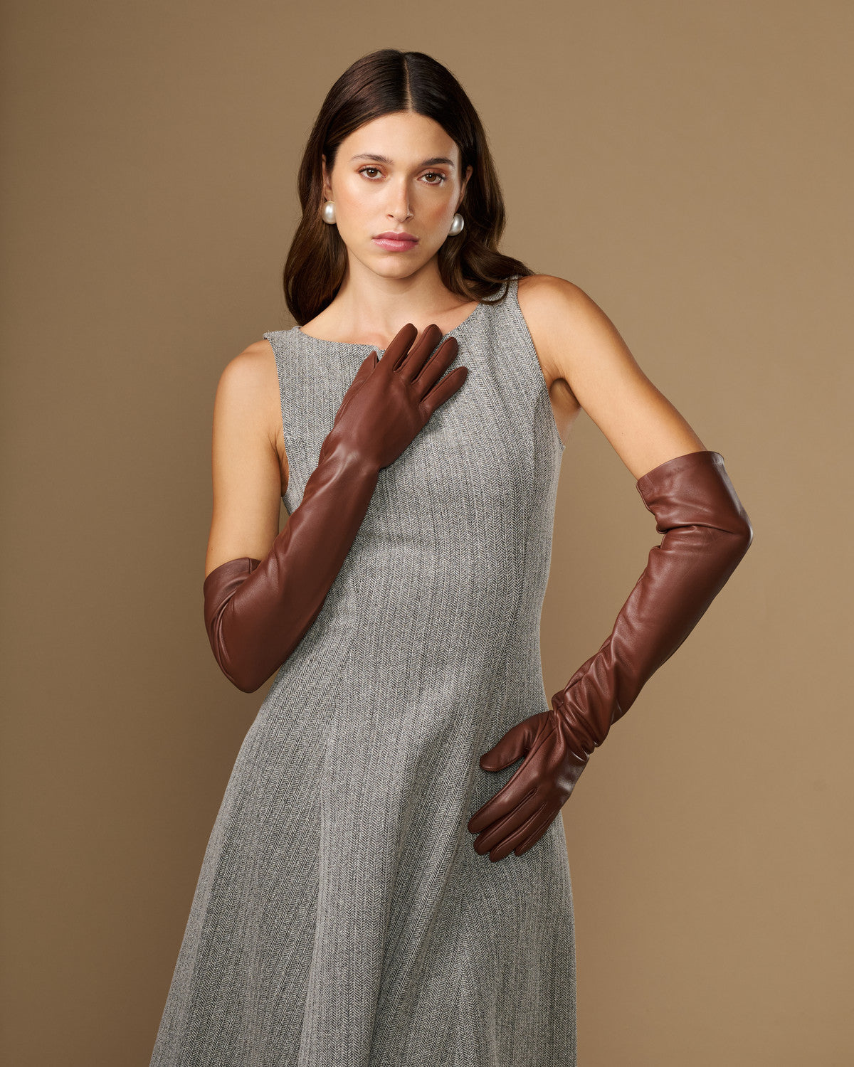 Women's chocolate-brown lambskin leather gloves, one hand raised with curved finger seams