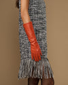 Women’s orange leather glove on raised arm, below-elbow length and tapered hand