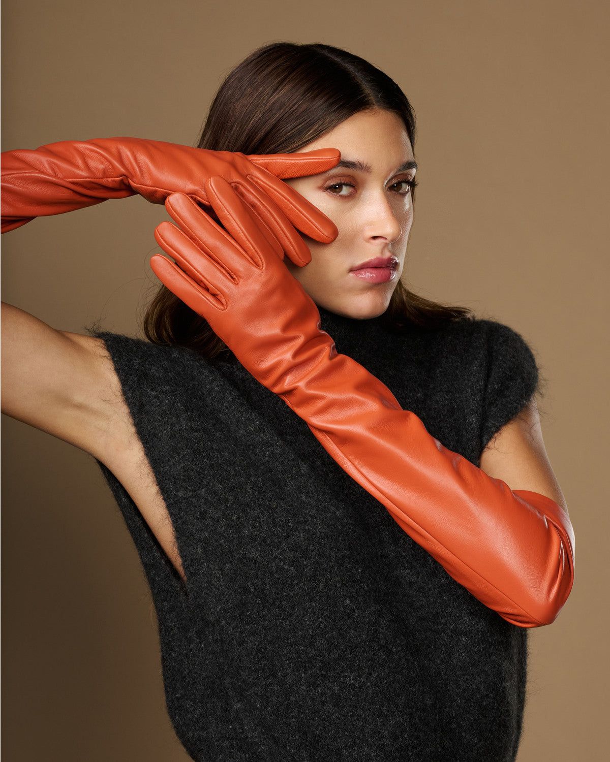 Orange lambskin leather gloves with silk lining and touchscreen tips, close-up on hands