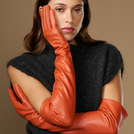Orange lambskin leather gloves with silk lining; touchscreen tips and seam details on hands