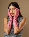 Pink women’s below-elbow leather gloves, fitted fingers, gloves held up near face