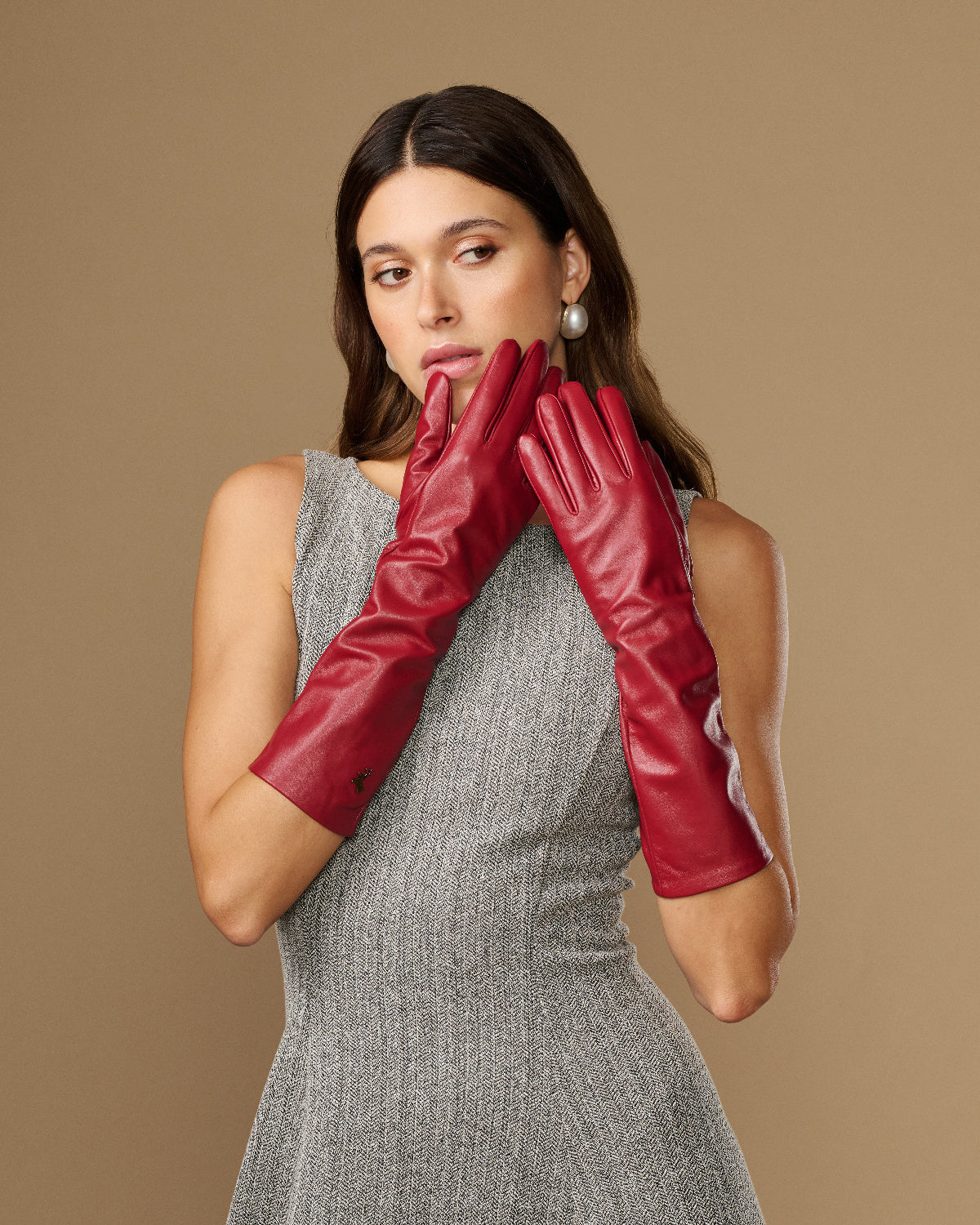 Red below-elbow leather gloves held together near face, showing glossy leather texture
