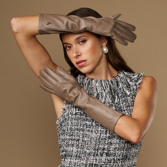 Taupe leather gloves with below-elbow cuff, smooth surface and stitched fingers on raised arms.