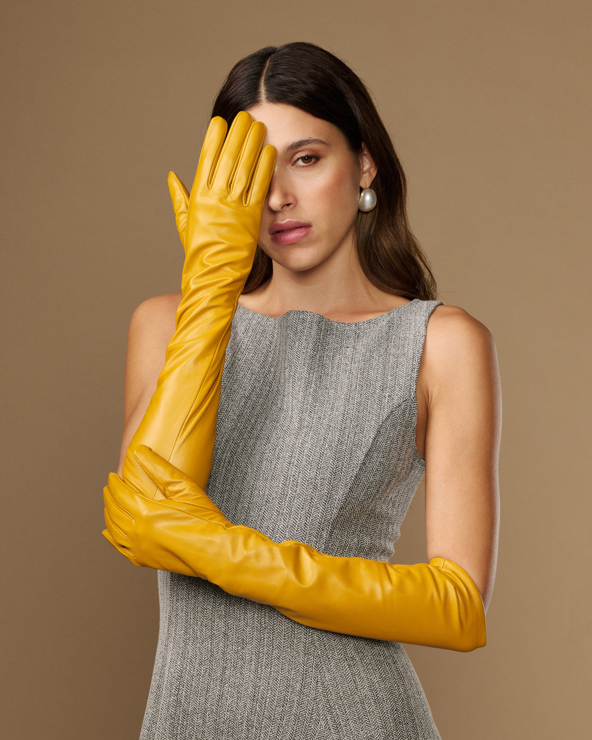 Yellow leather elbow gloves on model hands, one glove raised near face