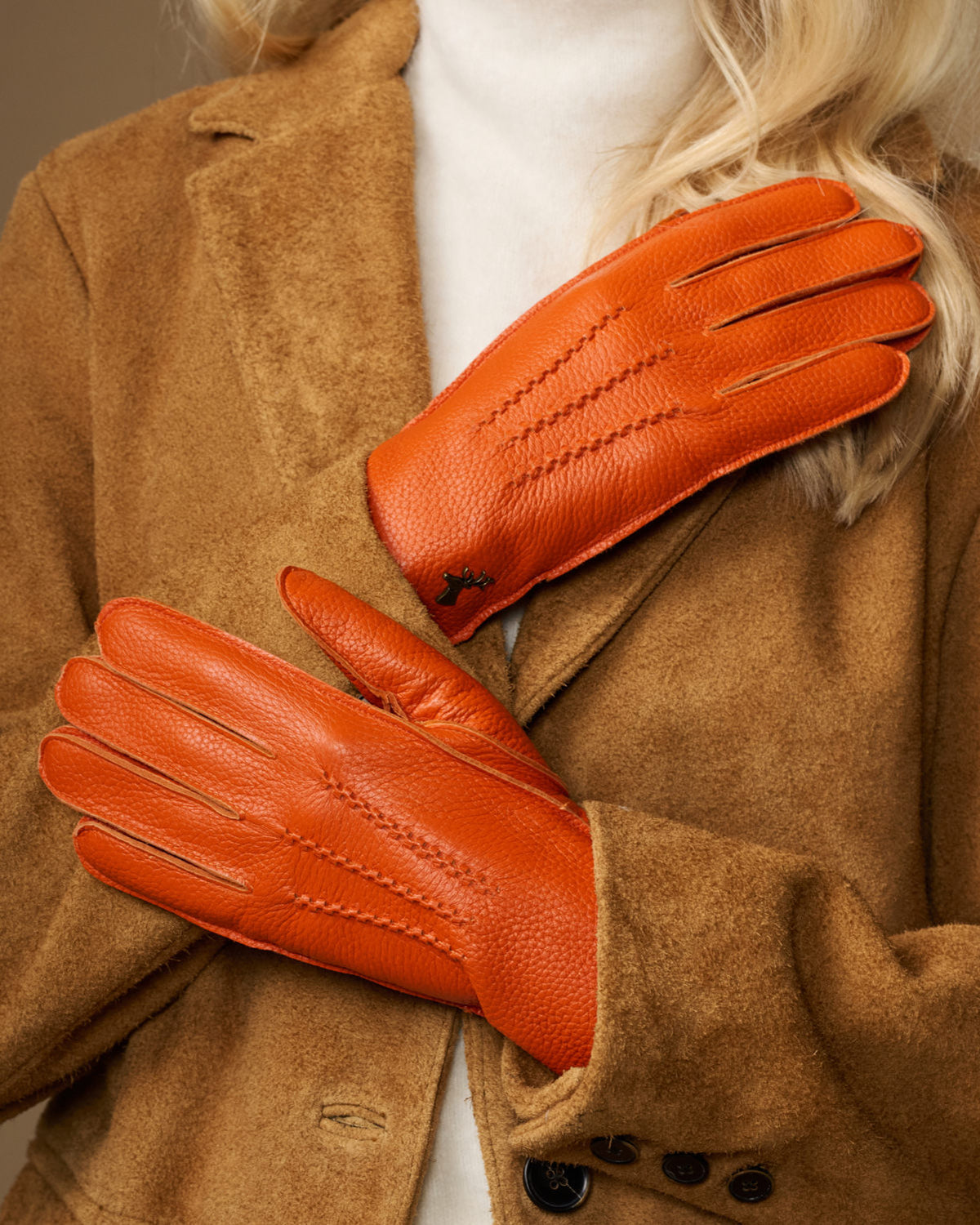 Orange leather gloves with stitched seams and soft lined cuffs, shown folded over sleeve